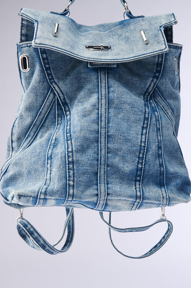 The KEEP EM ALL BACKPACK is a blue denim accessory with visible seams, silver hardware, and adjustable shoulder straps, shown against a plain light gray background. 4