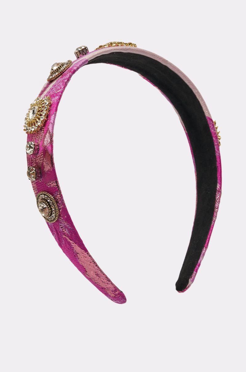 The GIRLS GIRL EMBELLISHED HEADBAND is a wide, pink metallic accessory with gold and silver jeweled accents, shown on a plain white background. 1