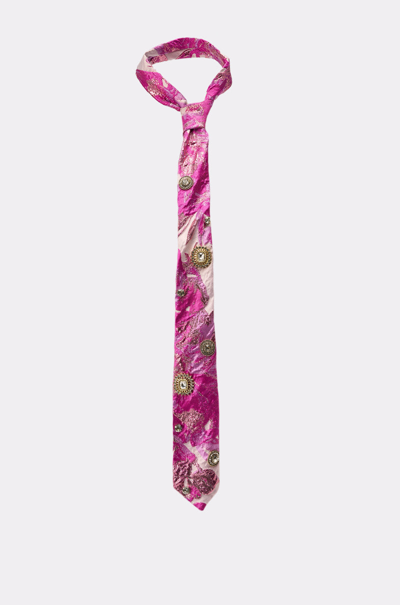 The GIRLS GIRL EMBELLISHED TIE is a pink statement accessory with circular floral patterns and abstract white accents, styled in a loose knot and shown against a plain light background. 3