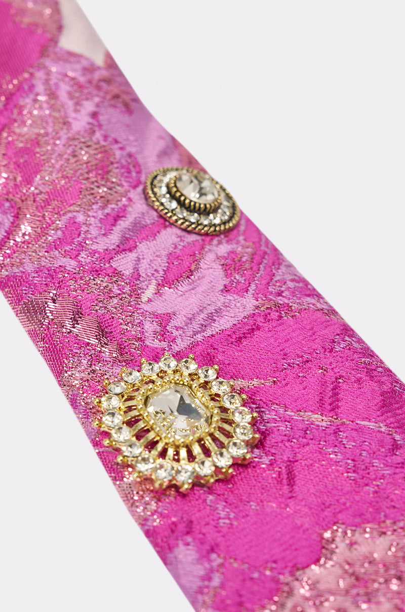 Close-up of pink and gold textured fabric with two brooches—one gold with clear gemstones, one silver with a central gem—perfect for accenting the GIRLS GIRL EMBELLISHED TIE. 5