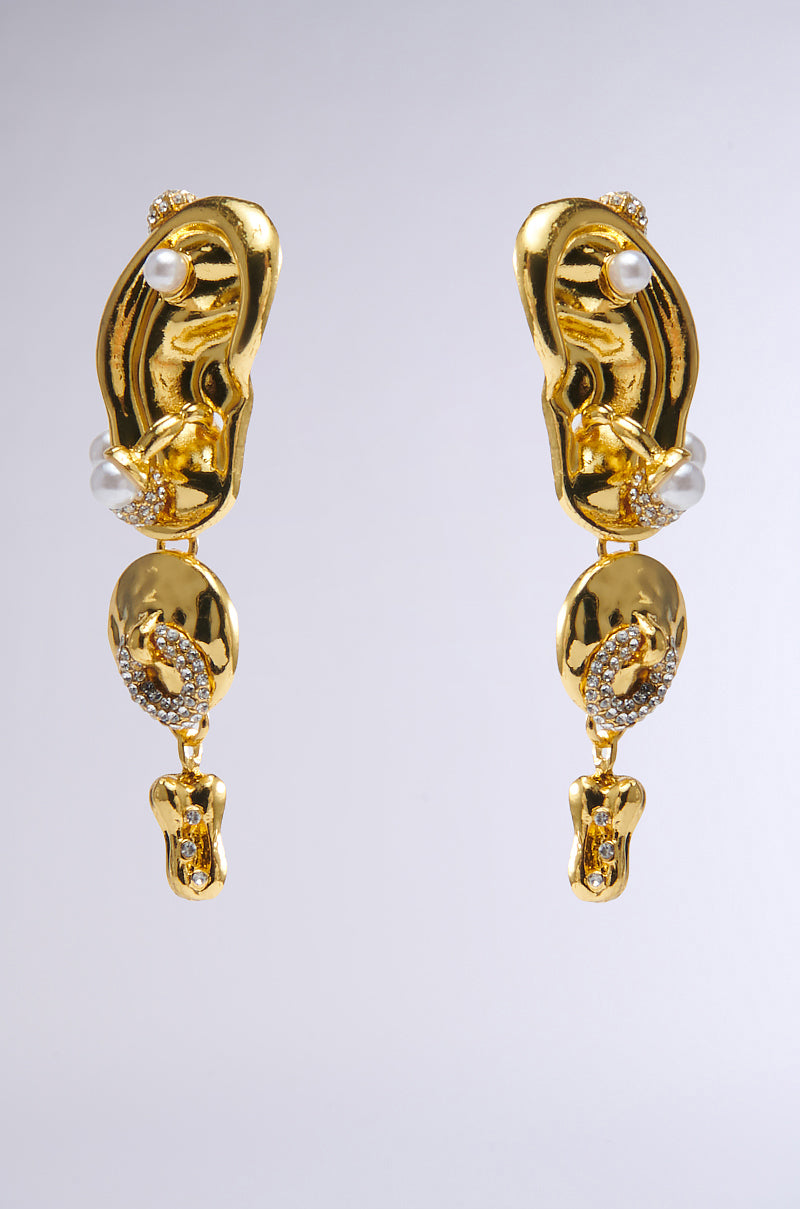 The HEAR ME OUT EARRING set features abstract, ear-shaped faux gold earrings with irregular forms, pearls, and rhinestone accents. Displayed against a grey background, they merge smooth and textured surfaces for a unique artistic look.