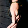 A hand with long, manicured nails rests on black fabric, showcasing the YOU COULD NEVER BRACELET—a sculptural piece that wraps around the wrist and thumb for a bold statement look.