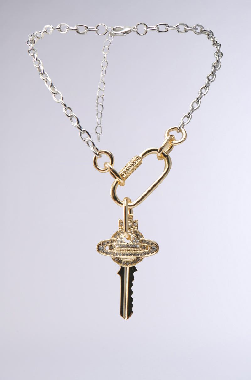 The TAKE ME AWAY NECKLACE features a chunky silver chain with a bold gold carabiner, accented by a key-shaped pendant showcasing a sparkling rhinestone planet orb and an elegant ring design. 0