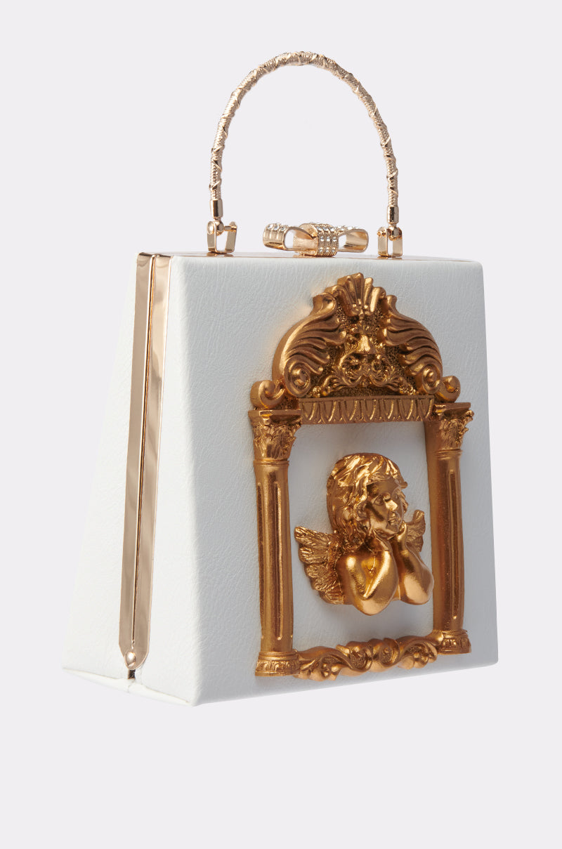 The IM AN ANGEL PURSE is a white trapezoidal faux leather bag with an ornate gold handle, a detailed gold frame, and a 3D cherub motif on the front, blending vintage glamour with Baroque art style. 2