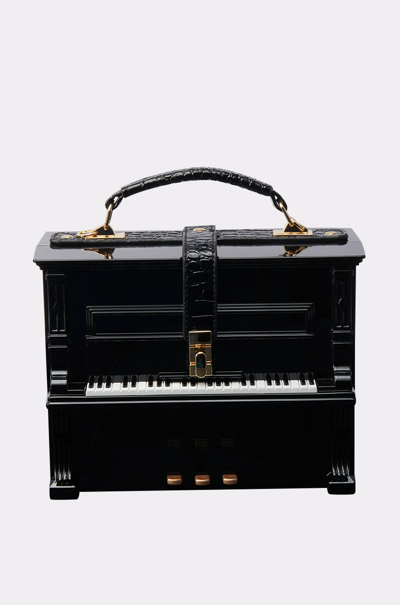 The PLAY ME PIANO PURSE is a black, grand piano-inspired bag with piano keys, a top handle, gold hardware, and a middle strap. It's part of the unique AKIRA Label collection.