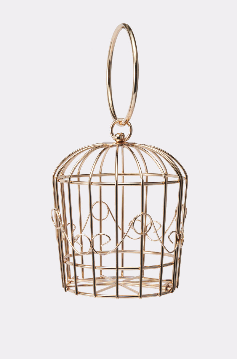The NEVER CAGED PURSE is a small, decorative gold wire birdcage bag with a round top, curved handle, and swirling side patterns, shown against a plain white background. 1
