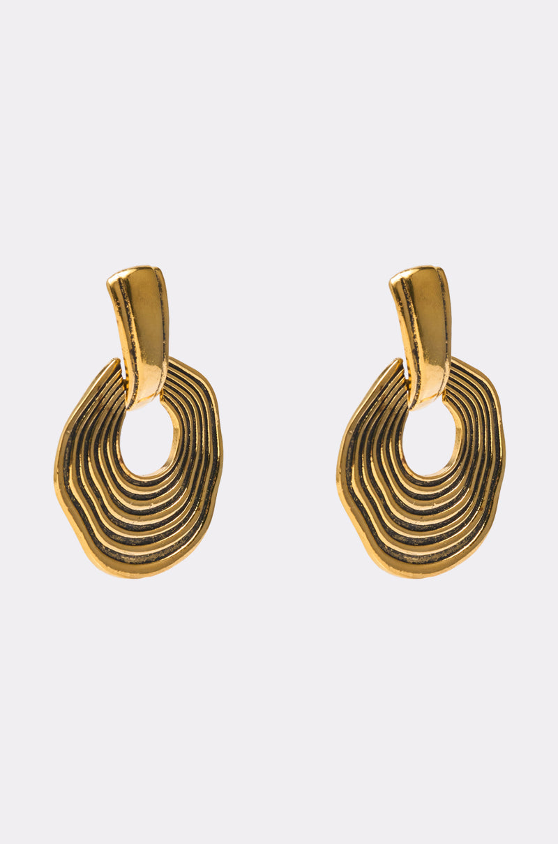 The SO WAVY EARRING is a pair of gold-toned statement earrings featuring a layered, irregular oval design with a smooth finish, shown against a light gray background. 2