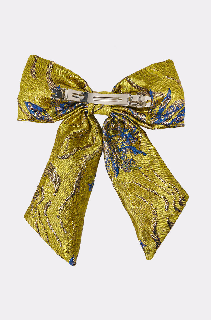 The LETS GO EMBELLISHED HAIR BOW is a gold brocade fabric accessory with blue and gold embroidery, shown from the back to highlight its metal fastening. 3