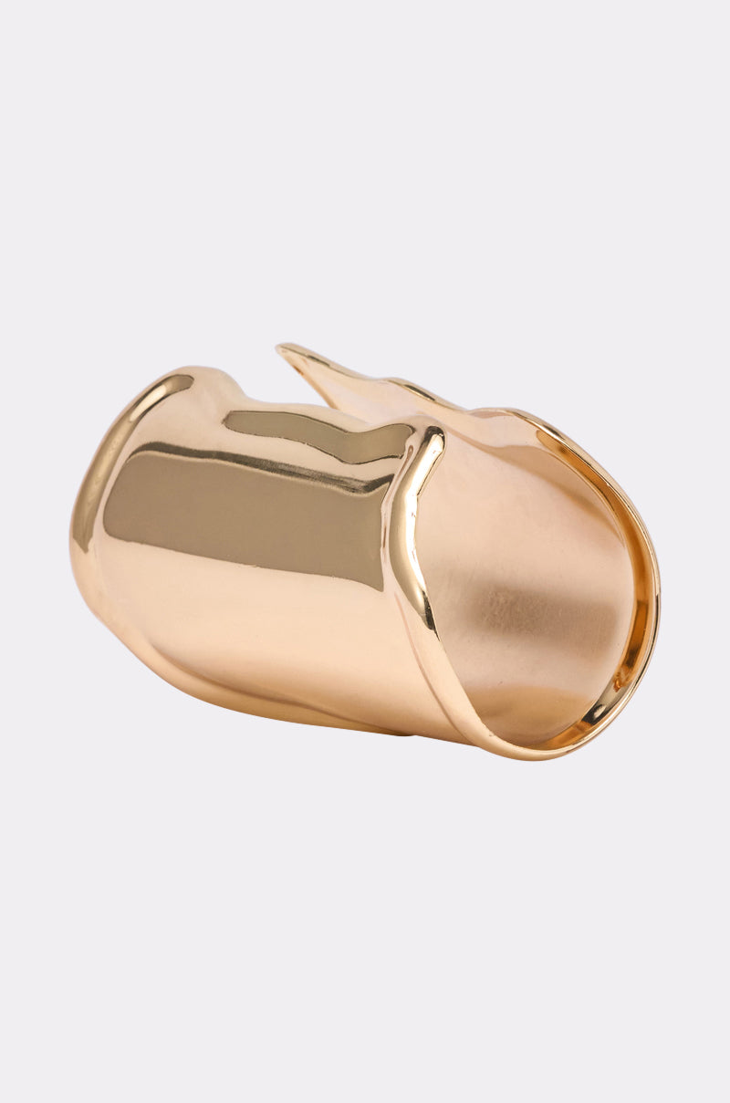 The OUTFIT COMPLETER CUFF features a shiny gold finish with a smooth, wide band and an asymmetrical, sculptural design, showcased against a light gray background. 3