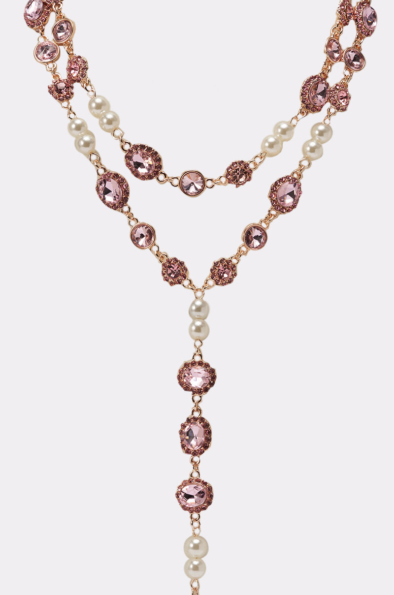 The UNDER THE LIGHTS NECKLACE is a vintage-inspired rose gold lariat featuring two strands with pink gemstones and white pearls in a striking Y-shape, making it an elegant accessory for any occasion. 2