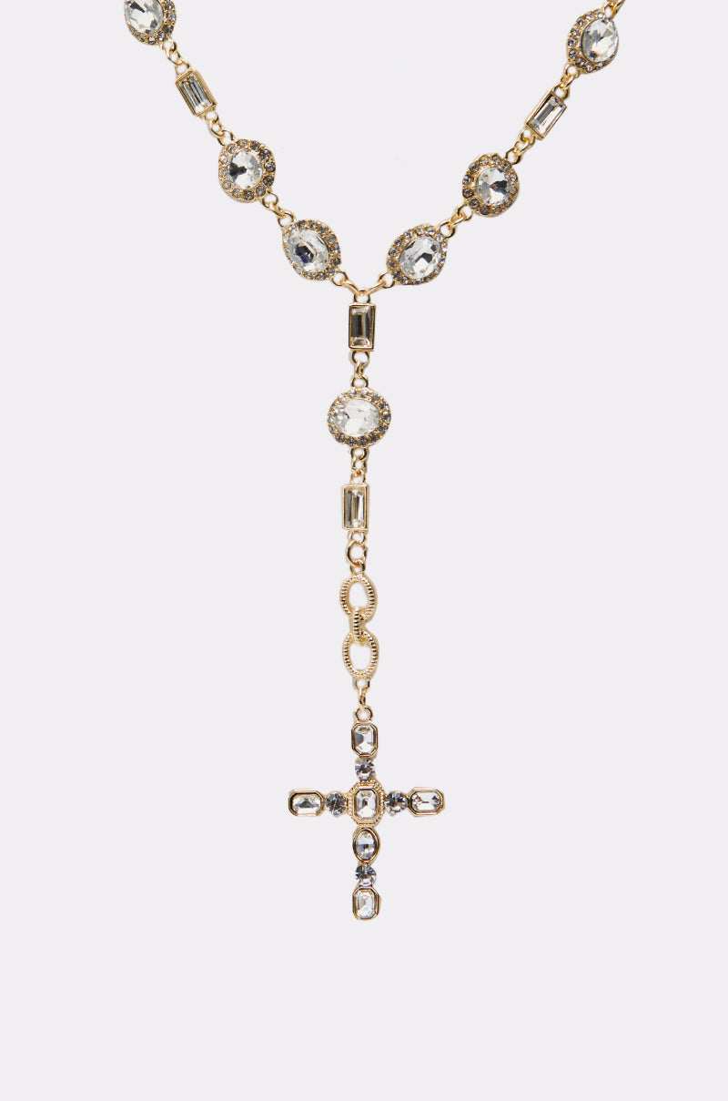 The TOTALLY CROSSED NECKLACE IN GOLD features a cross-shaped gold pendant adorned with clear gemstones, shown against a plain white background. 3