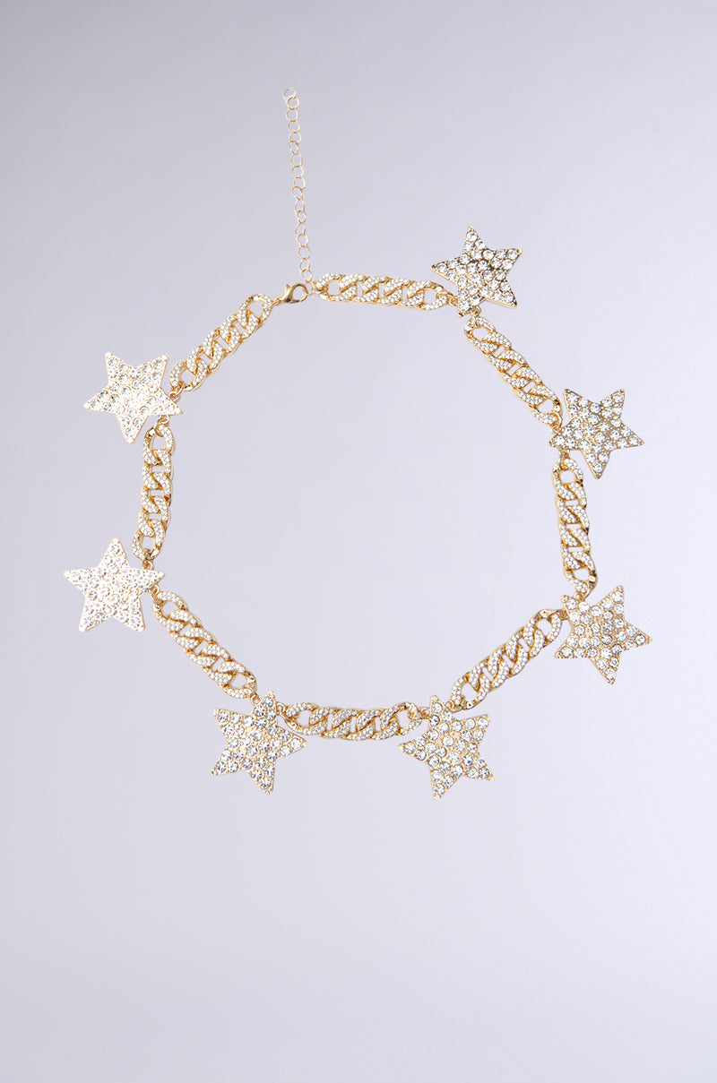 The GETTIN' STARSTRUCK NECKLACE IN GOLD showcases a chunky curb chain with rhinestone-studded star charms, beautifully displayed on a plain light gray background.