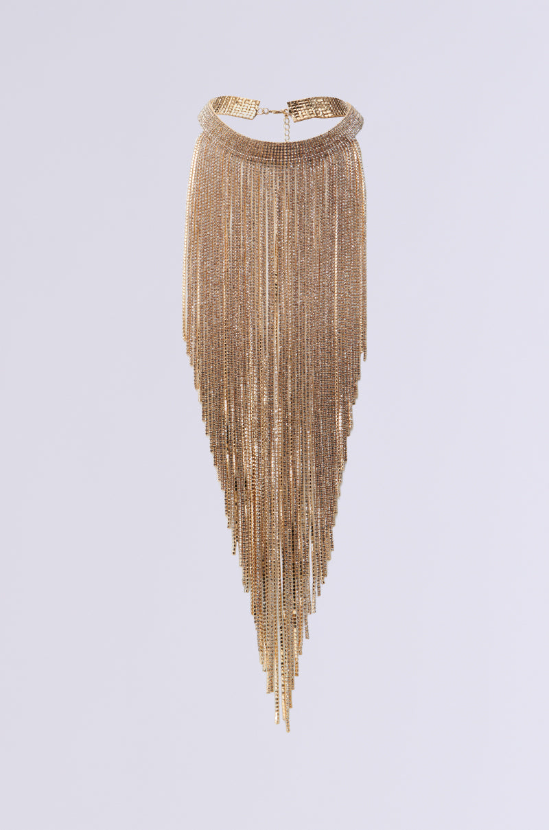 The IM A 10 NECKLACE is a rhinestone accessory that showcases a metallic faux gold design, featuring a wide textured band with cascading, layered chains forming a triangular shape, all set against a white background. 0