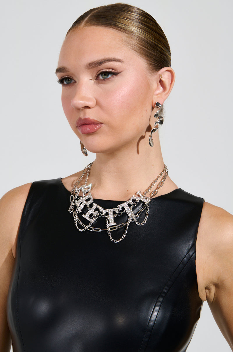 A woman with sleek hair wears a black leather top, statement earrings, and the "TOO PRETTY FOR THIS NECKLACE," a multi-layered silver rhinestone piece featuring intricate chain links. She gazes to the side against a plain background.