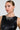 A woman with sleek hair wears a black leather top, statement earrings, and the 