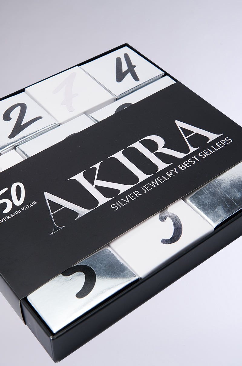 Box labeled "AKIRA Ultimate Jewelry Advent Calendar" with a modern design. This jewelry advent calendar features numbered sections from 1 to 9, embracing the holiday season in a silver and white color scheme.