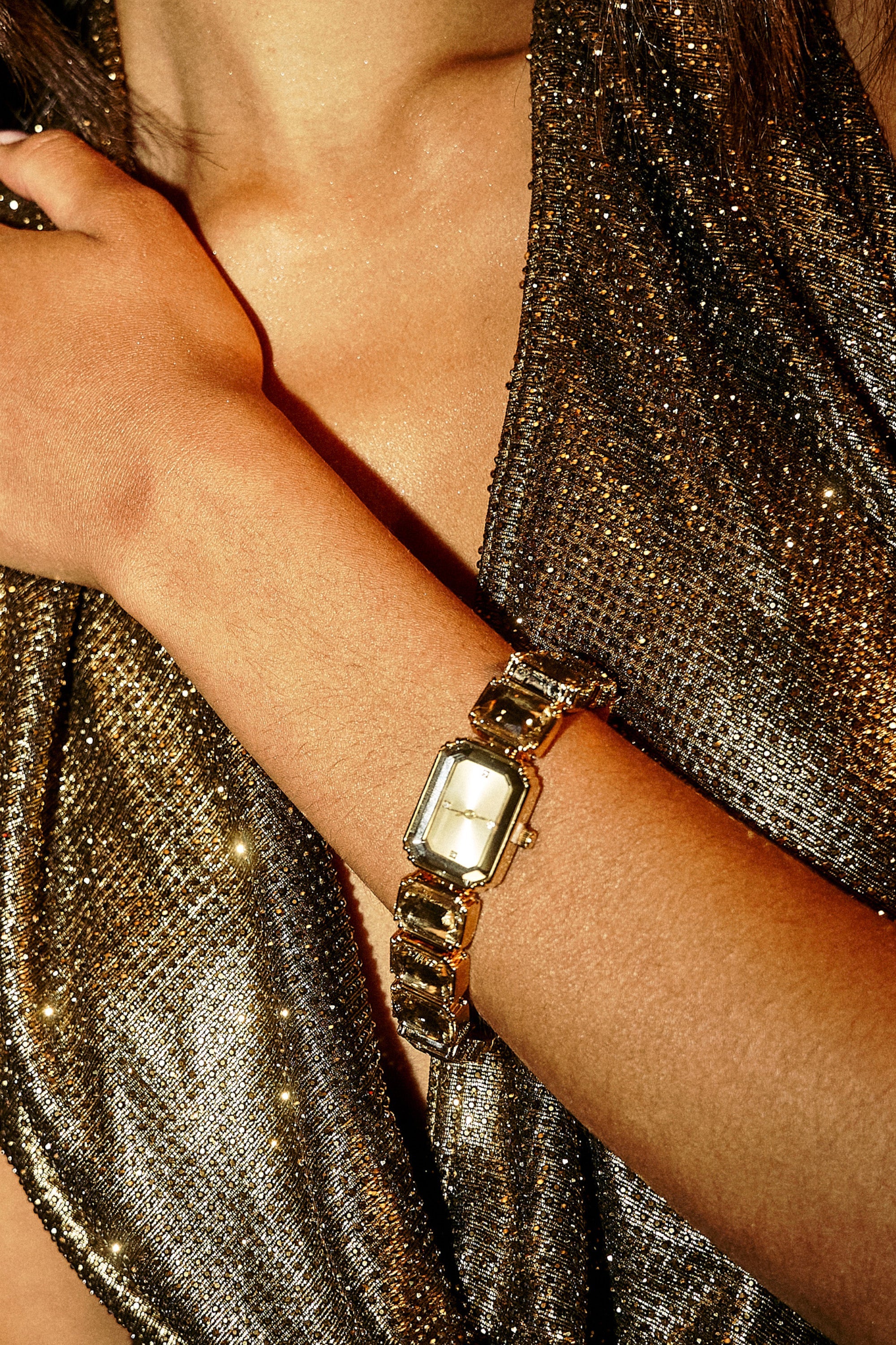 A person wears a sparkling metallic top and the SO GROOVY WATCH IN YELLOW, featuring a retro-chic rectangular gold band, with their hand resting gently on their shoulder. 0