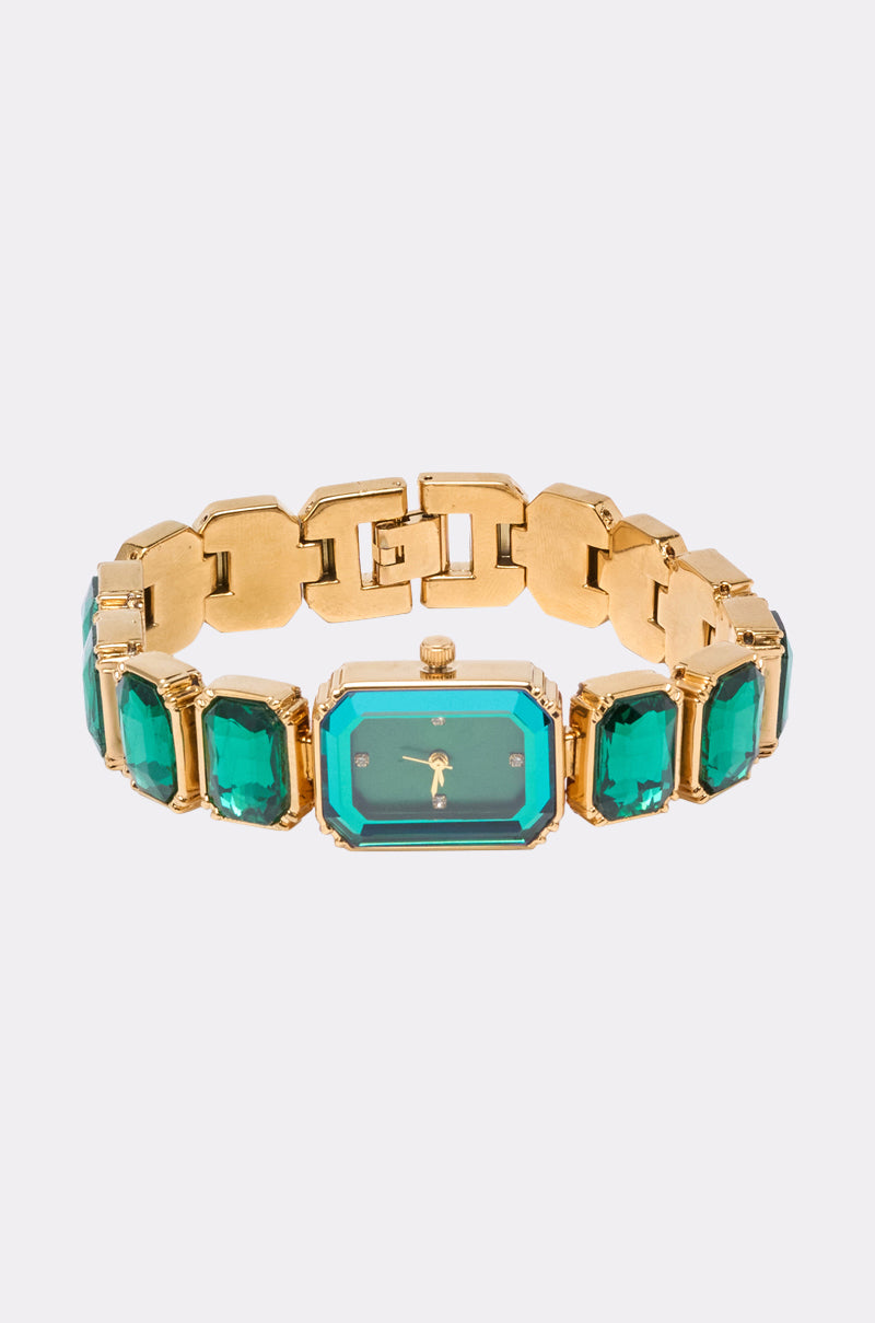 The SO GROOVY WATCH IN GREEN features a gold-tone metal case, a rectangular emerald-green gemstone face, and matching gemstone links, showcased on a light gray background. 3