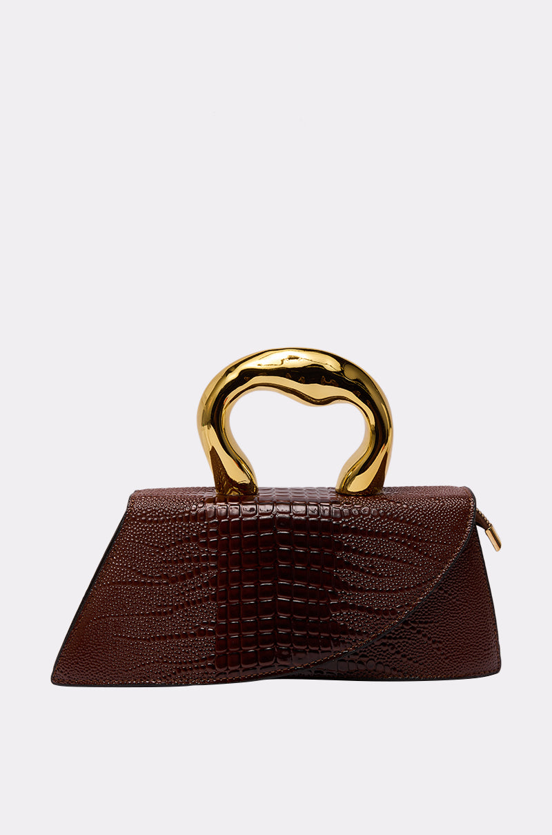 The DOESNT DESERVE ME PURSE is a brown bag with a textured reptile pattern, sculptural shiny gold handle, and detachable crossbody strap, shown against a plain light gray background.