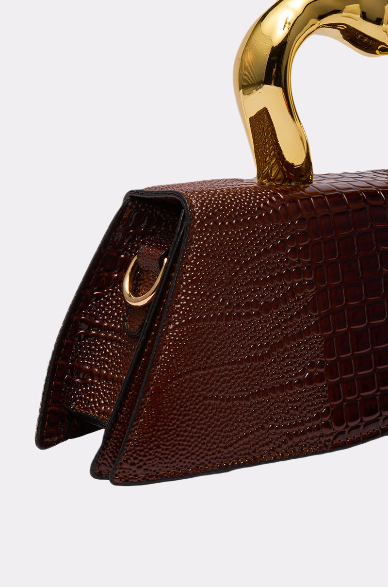 Close-up of the DOESNT DESERVE ME PURSE, a brown faux leather bag with an embossed reptile pattern, shiny gold handle, and small metal side ring, set against a plain light gray background.