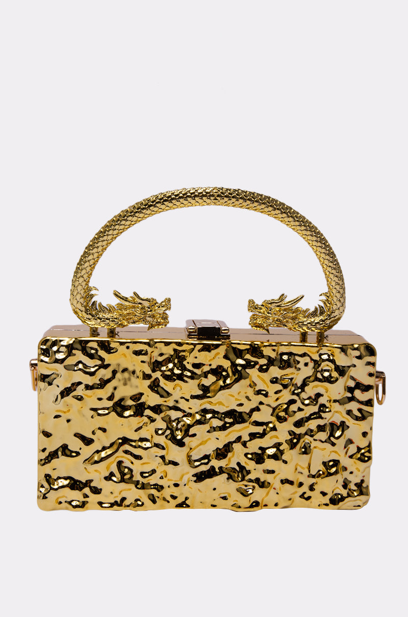 The MY KINGDOM CHROME PURSE is a metallic gold handbag with a hammered texture and dragon-shaped handle. Two dragon heads at the base add ornate luxury, making this a striking dragon handle bag. 1