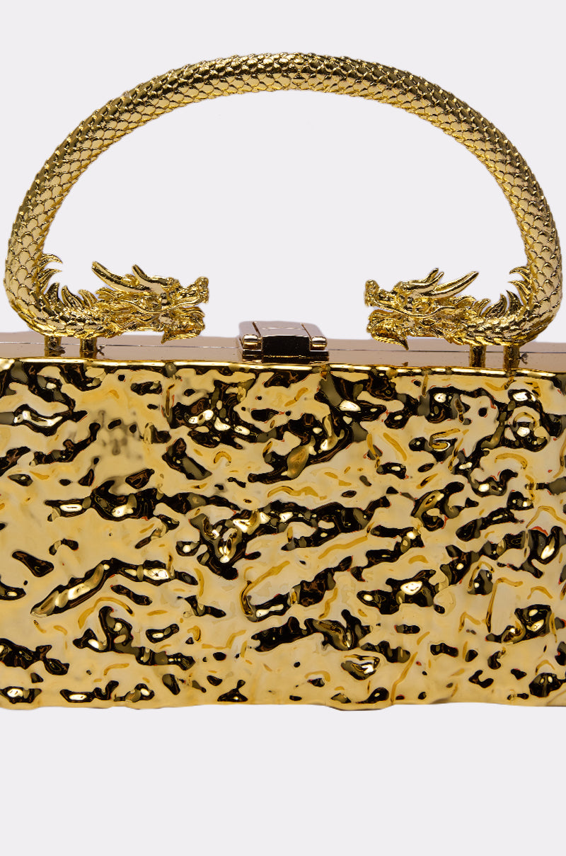 The MY KINGDOM CHROME PURSE is a shiny, textured gold handbag with a dragon-themed handle featuring two dragon heads facing each other at the clasp. 3