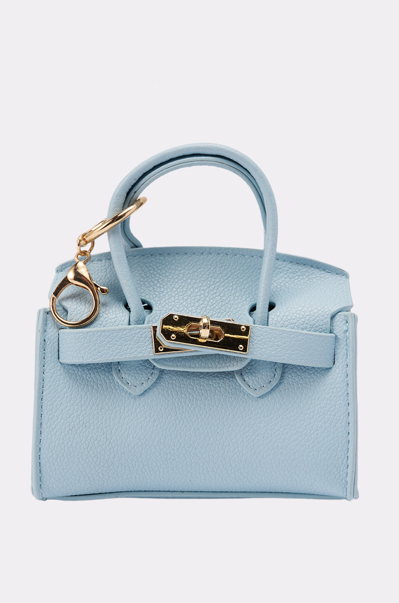 The NEVER TOO BIG BAG KEYCHAIN is a small light blue faux leather handbag with two handles, a gold clasp, and a purse-shaped keychain, shown against a plain white background. 1