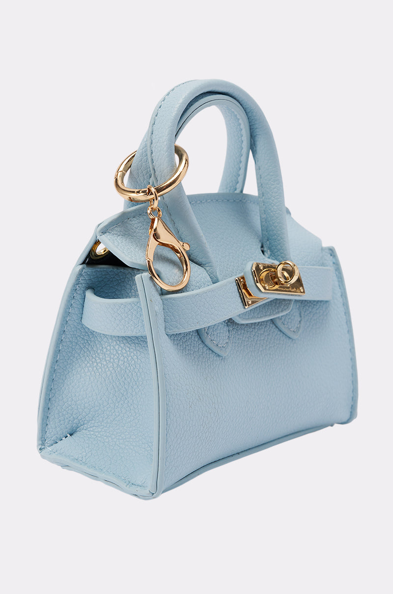 The NEVER TOO BIG BAG KEYCHAIN is a small light blue leather handbag with gold hardware, featuring a clasp and purse-shaped keychain, shown against a plain white background. 2