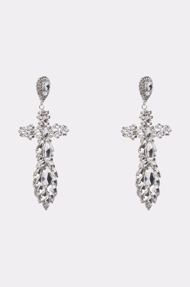 The WITH GRACE EARRING features ornate, oversized cross shapes in a silver-tone finish, embellished with clear rhinestones set in detailed floral and leaf patterns, displayed against a plain white background.