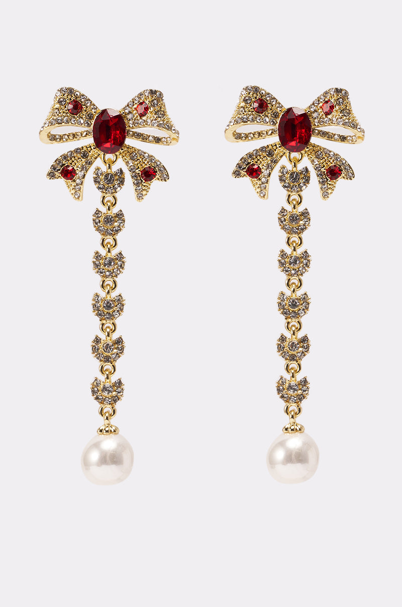 TIE WITH A BOW EARRING featuring gold bows, red gemstones, a delicate dangling gold chain, and a faux pearl drop, displayed on a light background. 0