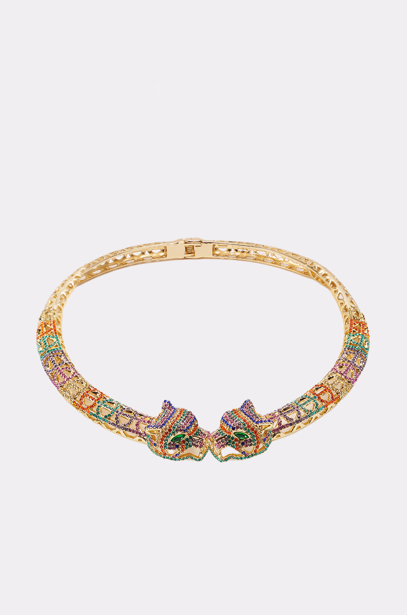 The LUXE JAG NECKLACE is a gold-tone statement choker adorned with colorful gemstones and two stylized jaguar heads facing each other at the center. 0