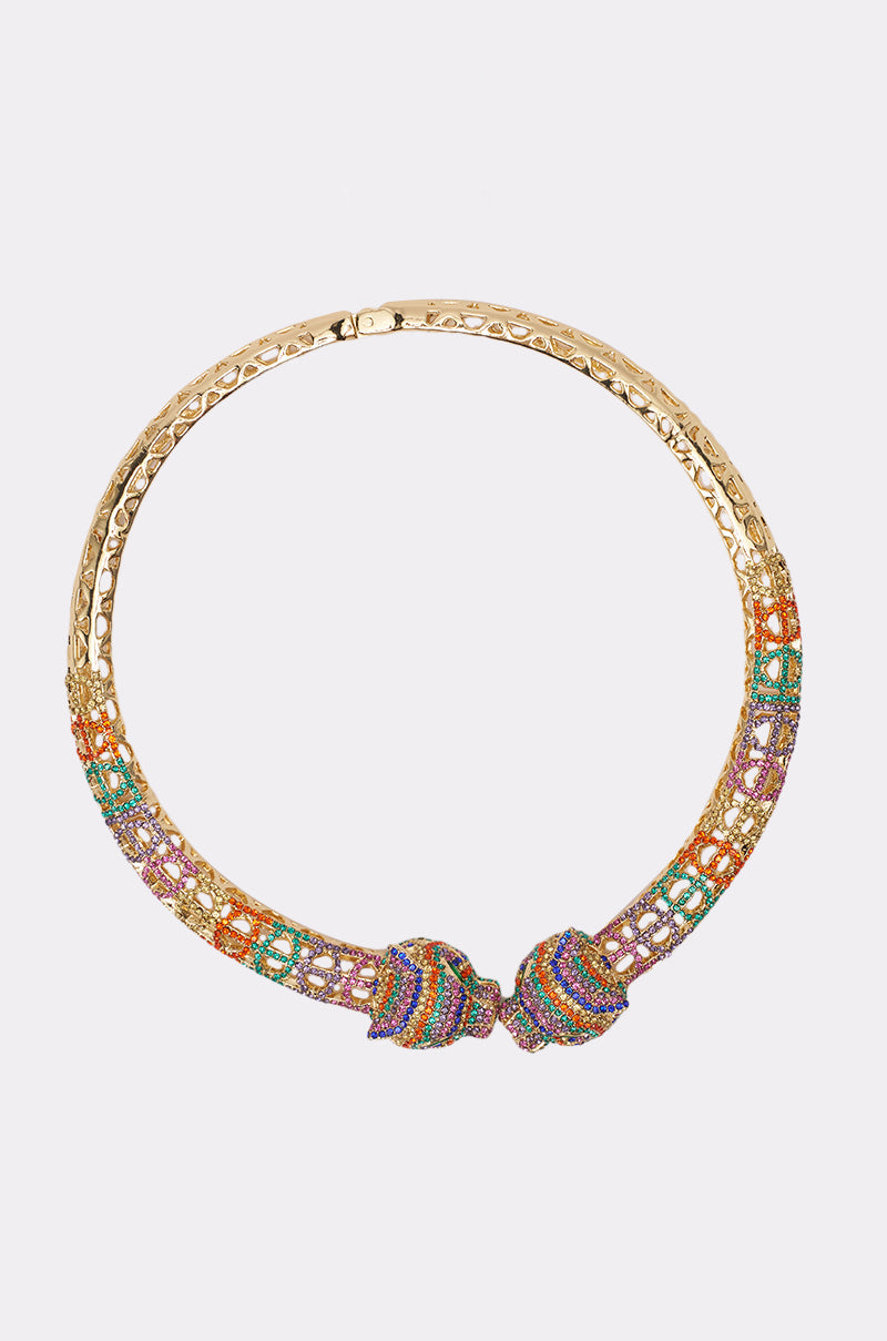 The LUXE JAG NECKLACE is a gold choker with intricate latticework, vibrant gemstones in bold patterns, and two decorative front knots—a true statement piece. 1