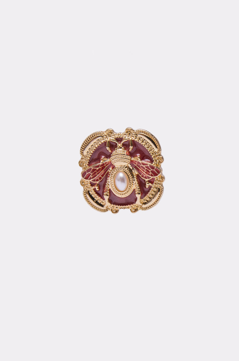 The DESI EARRING is a gold ornate piece featuring a detailed bee design with red wings and a central faux pearl, displayed on a plain white background. 3