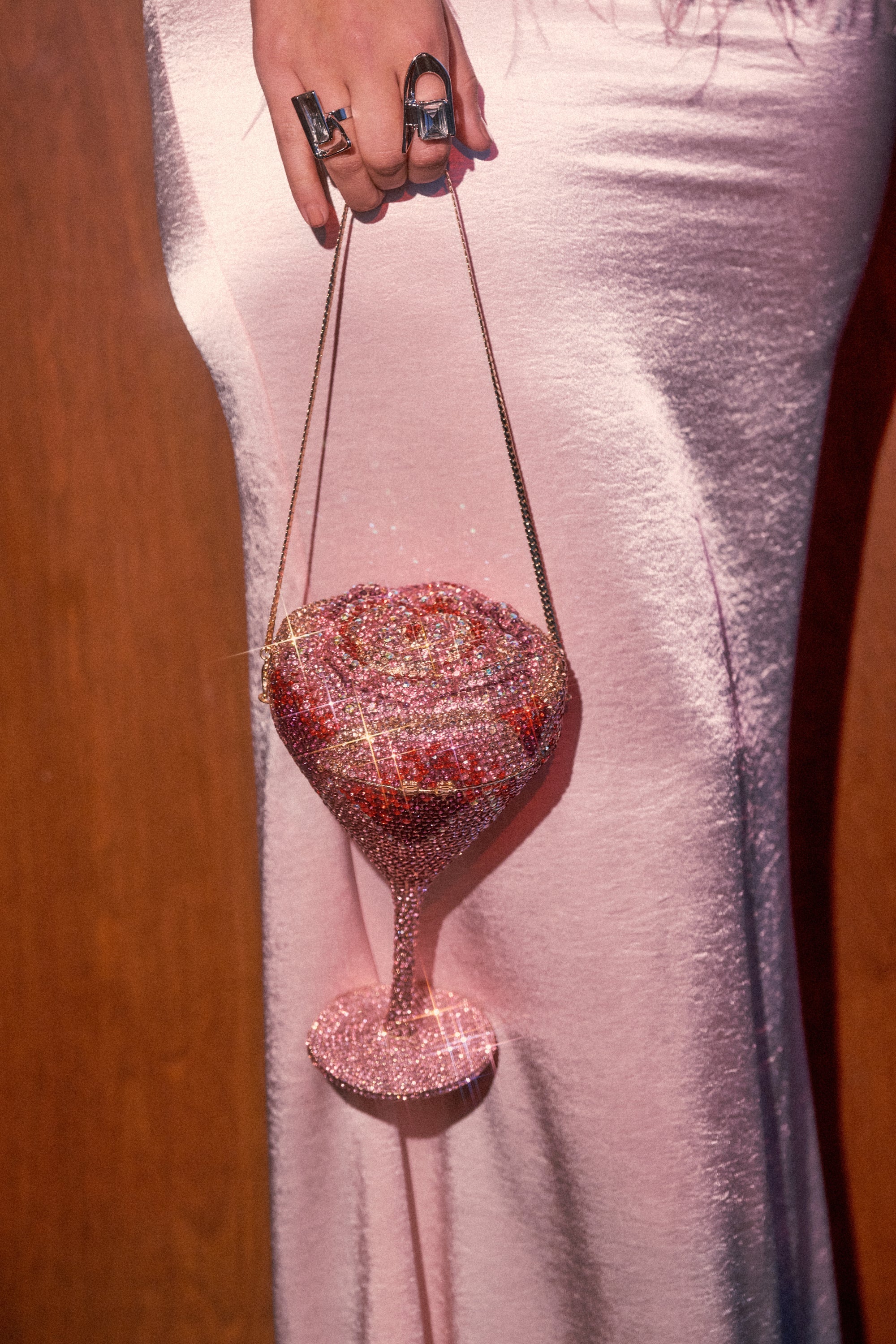A person in a pale pink satin dress holds the TAKE A SIP BLING PURSE—a sparkling martini glass-shaped bag featuring a rose motif, gold chain strap, and glittering rhinestones for ultimate statement style. 2