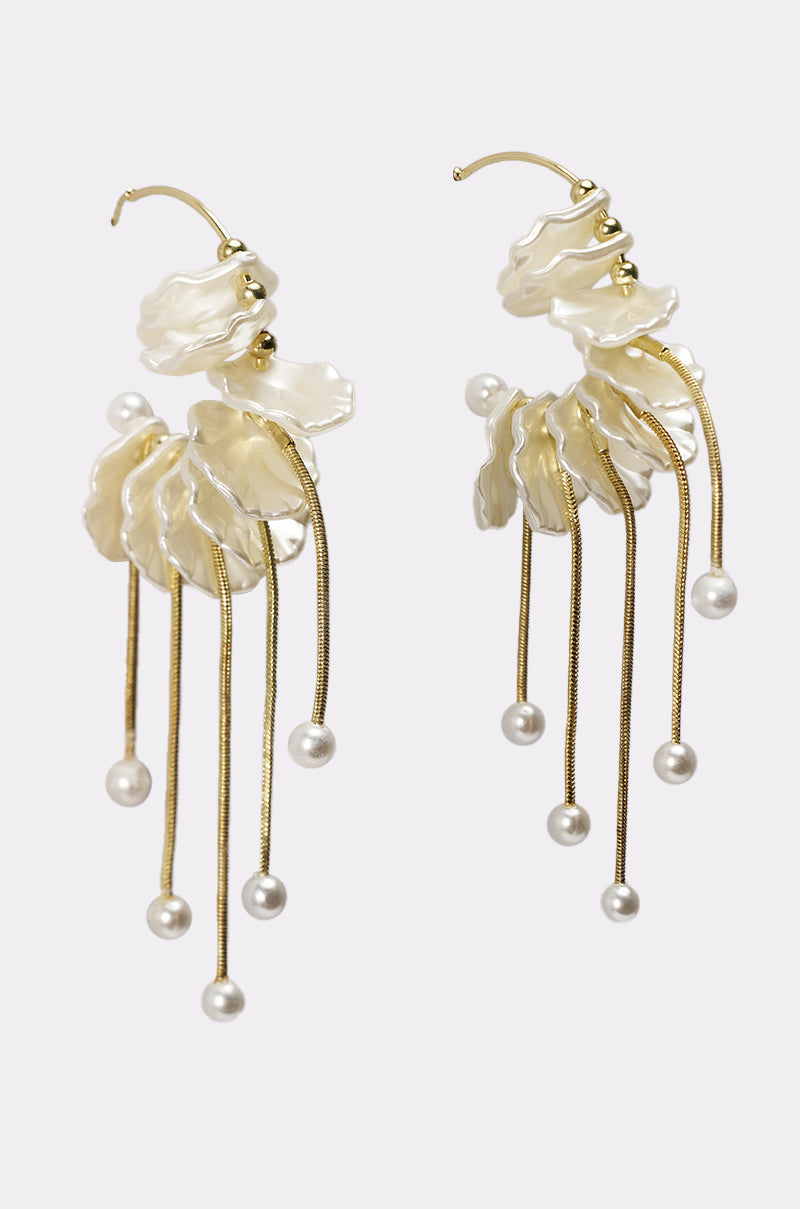 The KYLA EARRING features gold-tone hoops with layered petal-like white accents and dangling thin gold chains, each ending in a round white pearl bead, displayed on a plain white background. 0