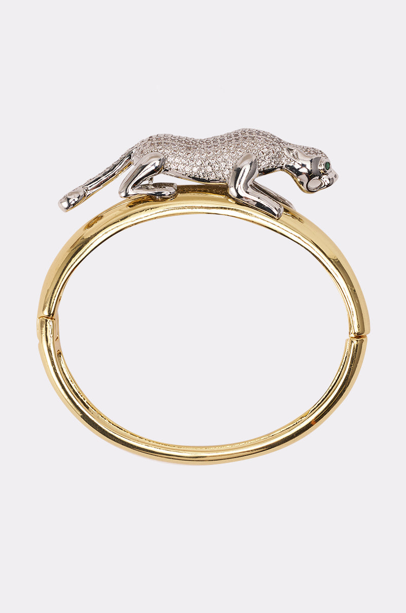 The JUMP ON IT BRACELET is a gold-tone bangle featuring a prowling silver panther with green gemstone eyes and shimmering rhinestones—an elegant statement piece and dazzling panther accessory in one. 0