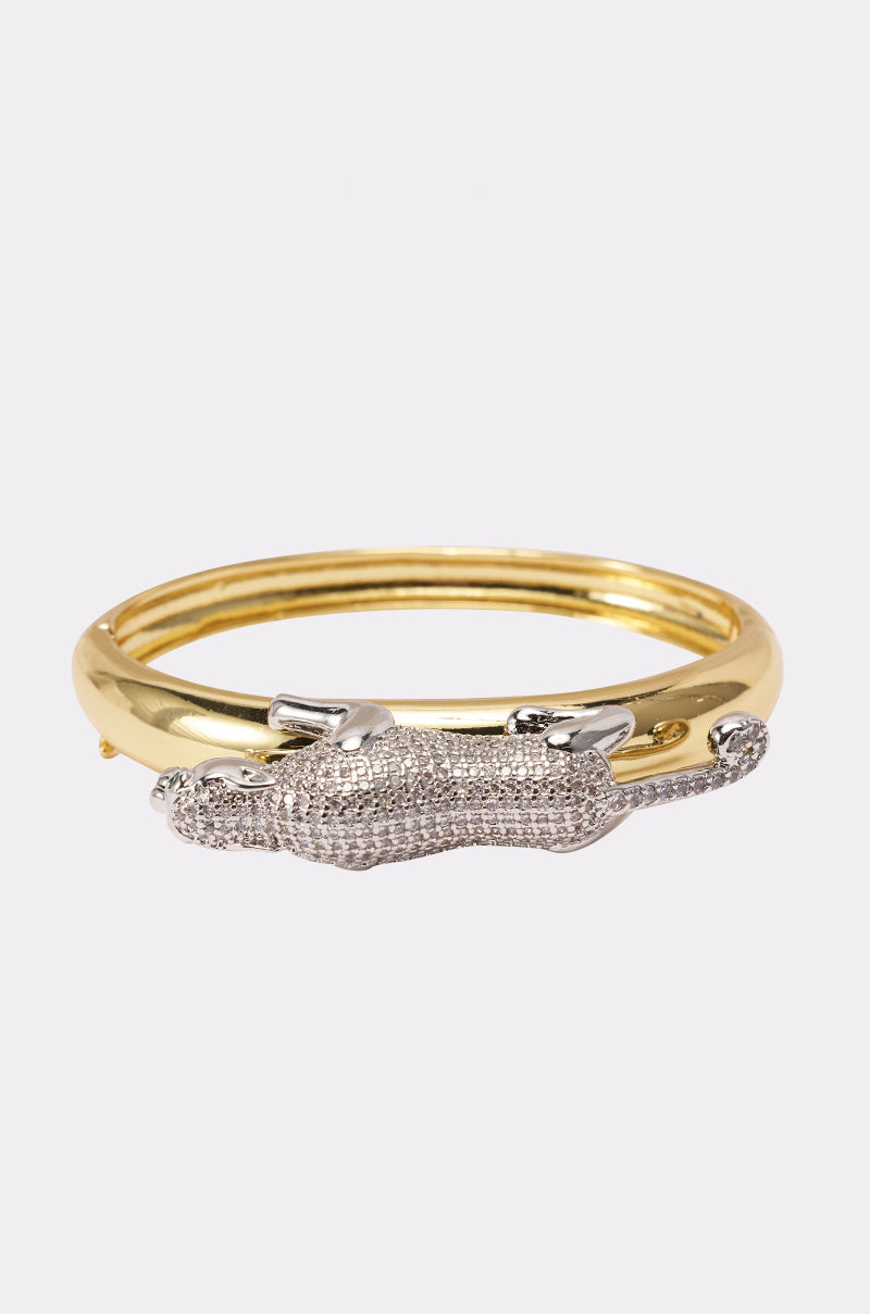 The JUMP ON IT BRACELET is a sculptural gold bracelet featuring a detailed silver, diamond-encrusted panther figure stretched across the top, shown against a plain white background. 2