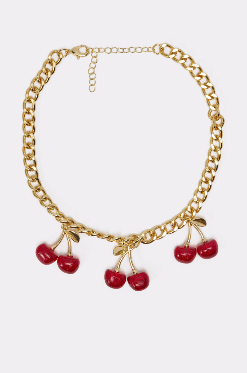 The POP IT NECKLACE features a chunky chain with three red cherry pendants, each detailed with gold stems and leaves, channeling playful Y2K vibes. The cherry charm necklace is set against a plain white background. 1