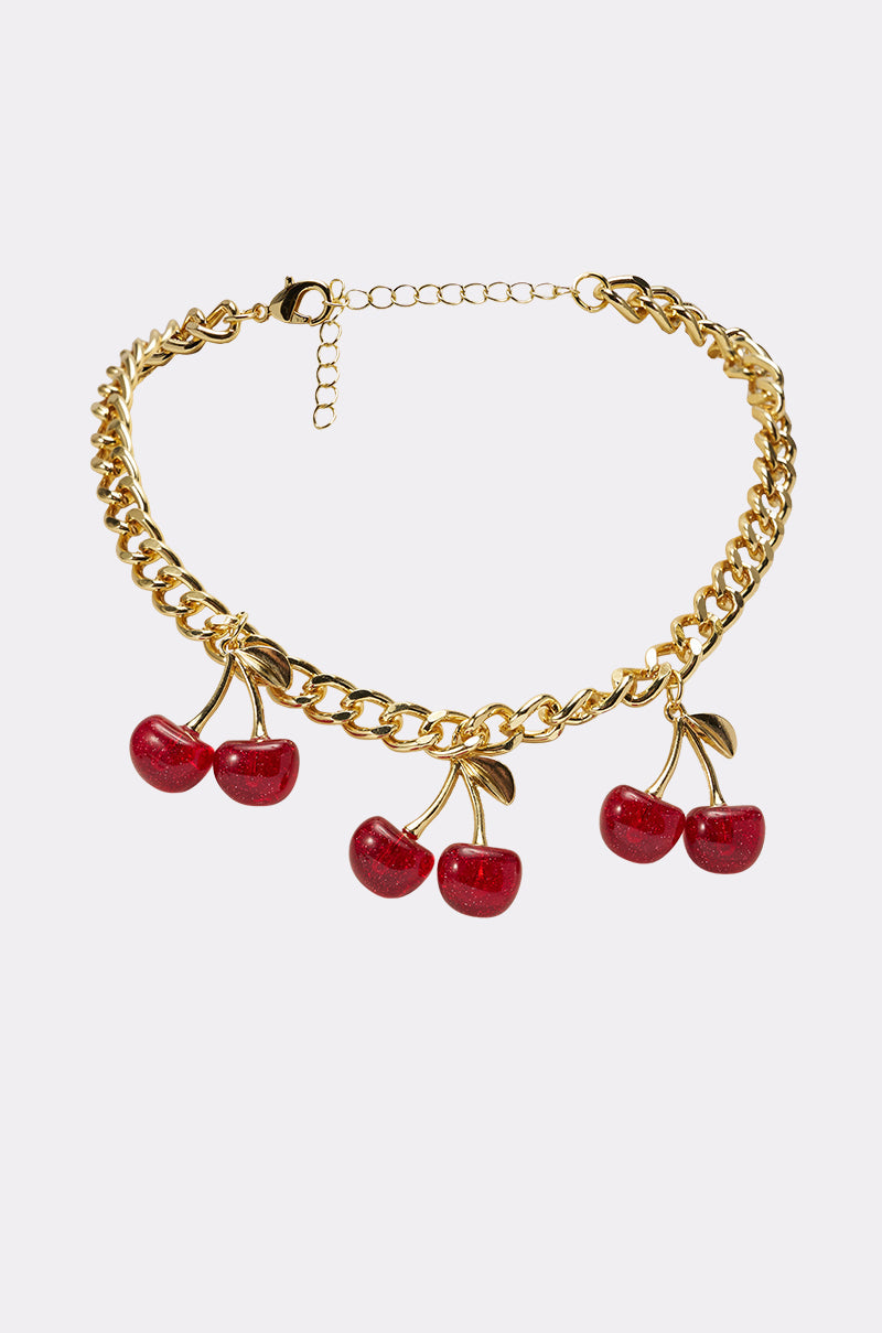 The POP IT NECKLACE is a Y2K-inspired chunky chain adorned with three red cherry charms, each with golden stems and leaves, showcased against a plain light background. 2
