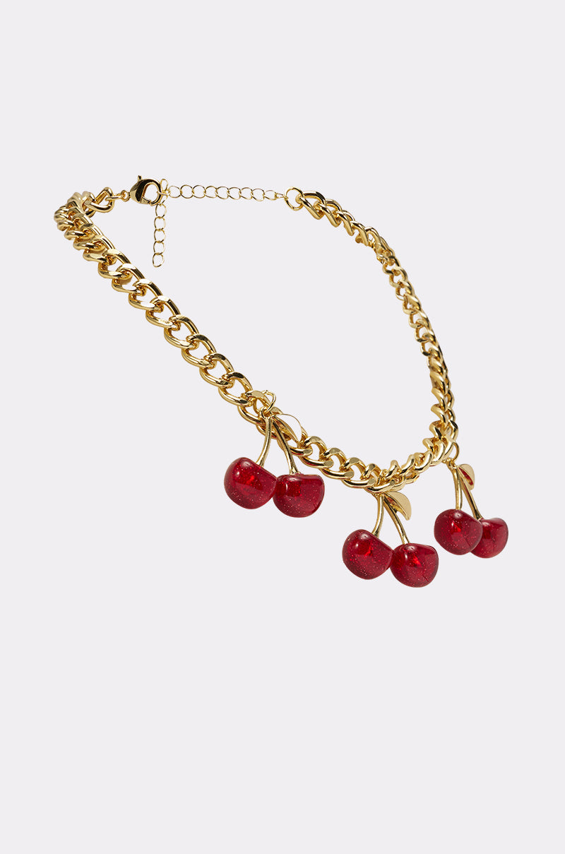 The POP IT NECKLACE is a gold-tone chain necklace featuring three pairs of red cherry charms, shown on a plain white background. 3