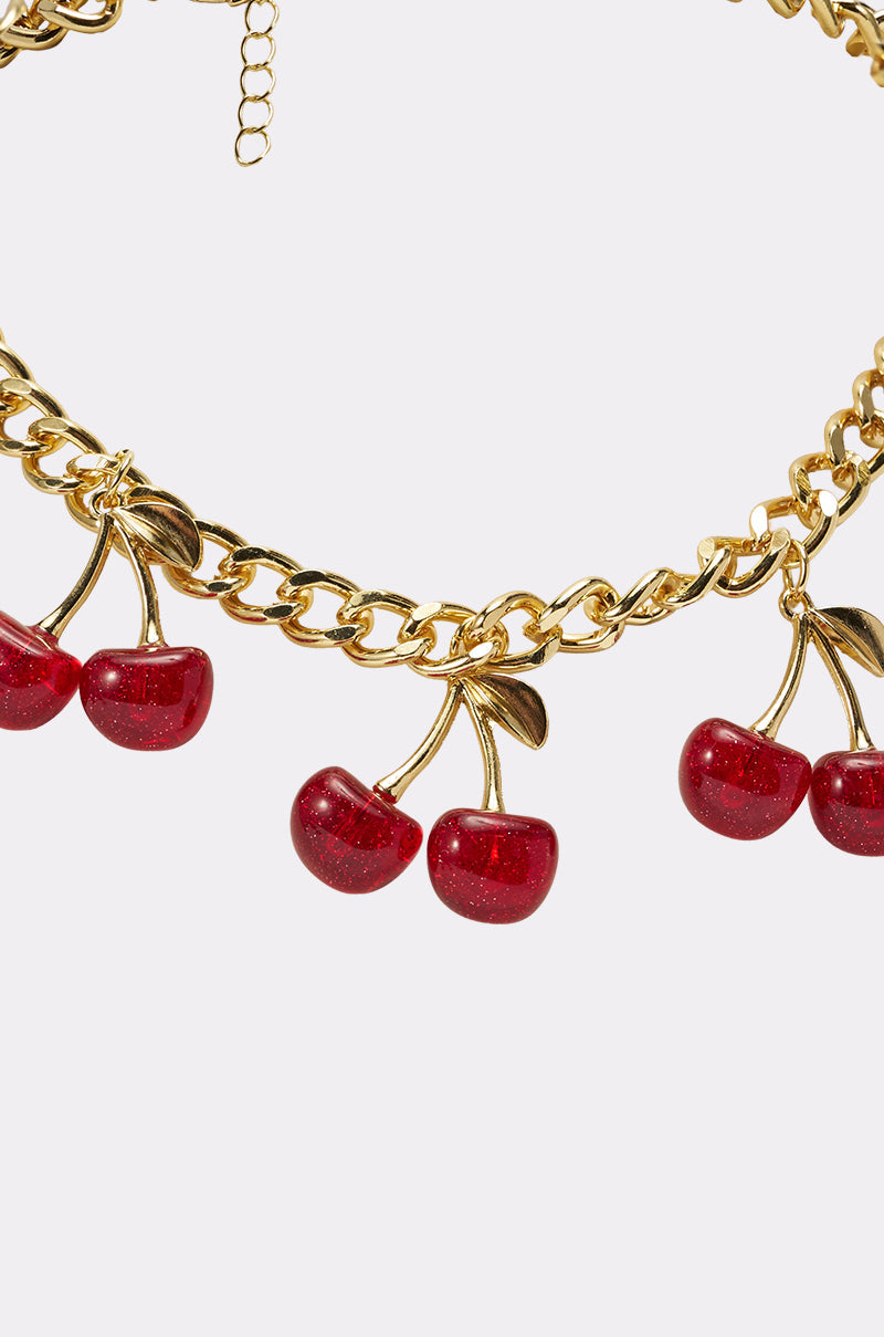 The POP IT NECKLACE is a gold-tone chain adorned with red cherry charms and green leaves, evenly spaced for a playful Y2K vibe—perfect for adding a vibrant pop of color to any look. Displayed on a plain light background. 4