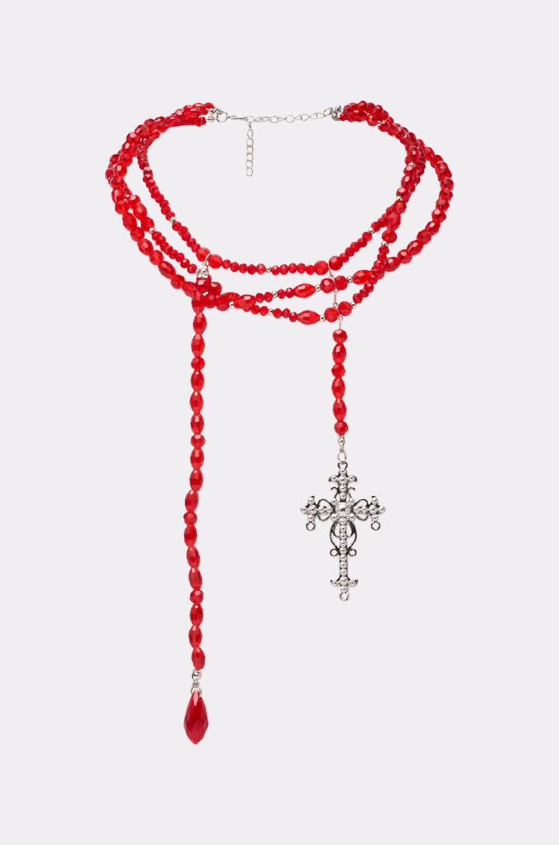 The TRIPPIE CROSS NECKLACE features layered red beads, an ornate silver cross pendant, and a single red teardrop bead, all displayed against a light background. 2