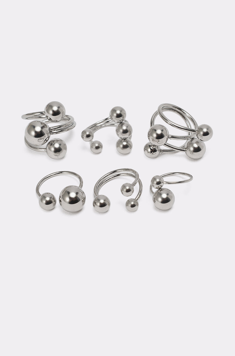 The MOD GAL RING SET features seven silver-tone stacking rings with minimalist open ends, each topped with smooth, shiny spheres in varying sizes—arranged on a light grey background for the perfect minimalist jewelry set. 2