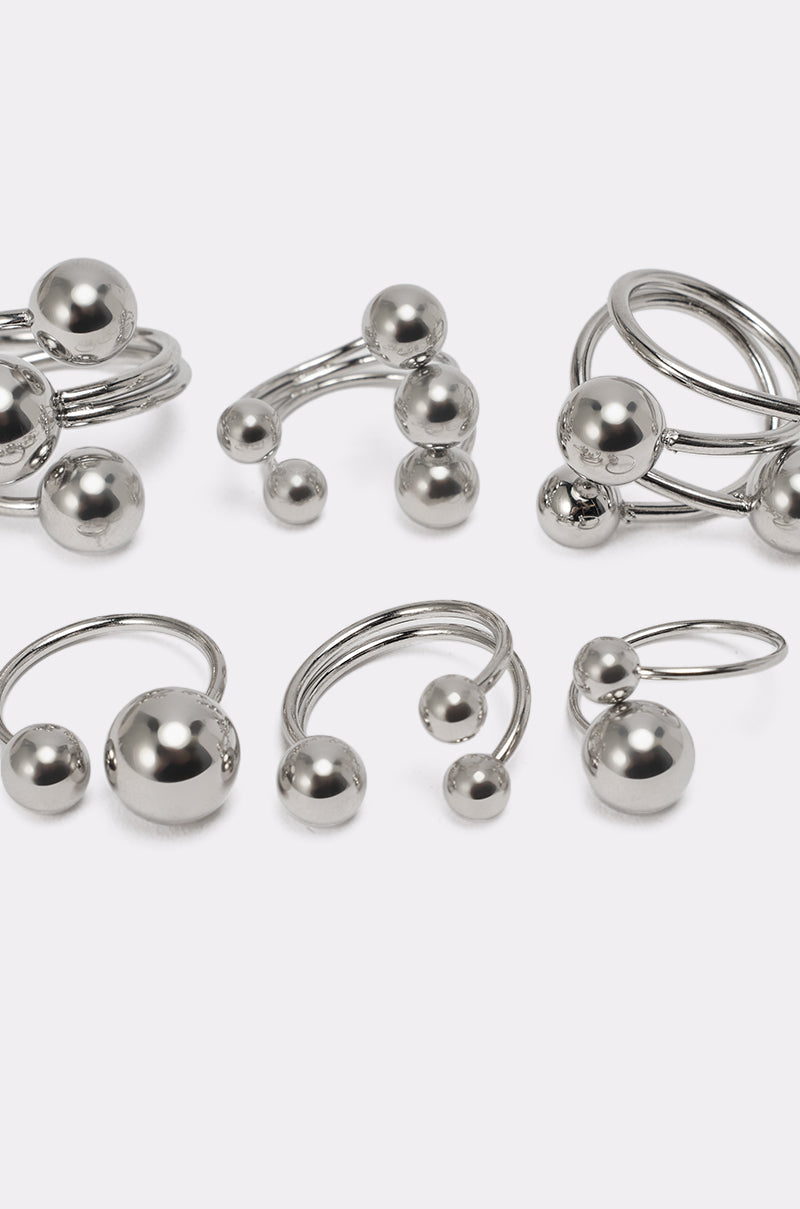 The MOD GAL RING SET features silver-tone stacking rings adorned with metallic spheres in various sizes, showcasing minimalist and modern designs with smooth, shiny finishes on a plain white background. 5