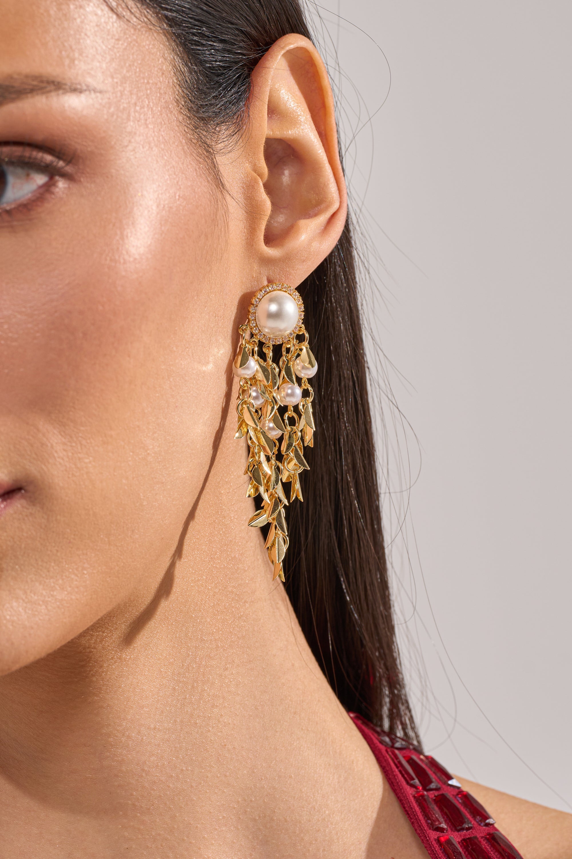 Close-up of a woman's ear wearing the PARADISE EARRING—elegant gold leaf design with pearl accents, ideal as wedding earrings. She has straight dark hair, wears a red top, and only part of her face is visible. 5