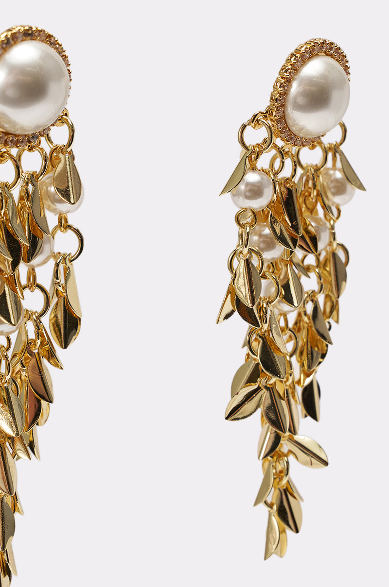 The PARADISE EARRING features large faux pearls and cascading gold charms on multiple chains. These elegant pearl drop earrings offer a luxurious design, ideal for weddings, shown against a plain white background. 4