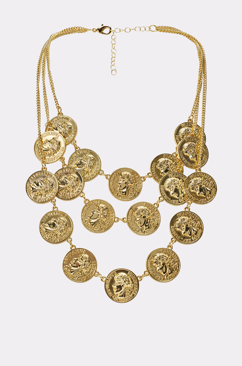The IN MY BAG NECKLACE is a layered gold-tone coin necklace with three chains, each featuring large medallion charms embossed with unique portraits and designs. An adjustable clasp at the top ensures a perfect fit. 0