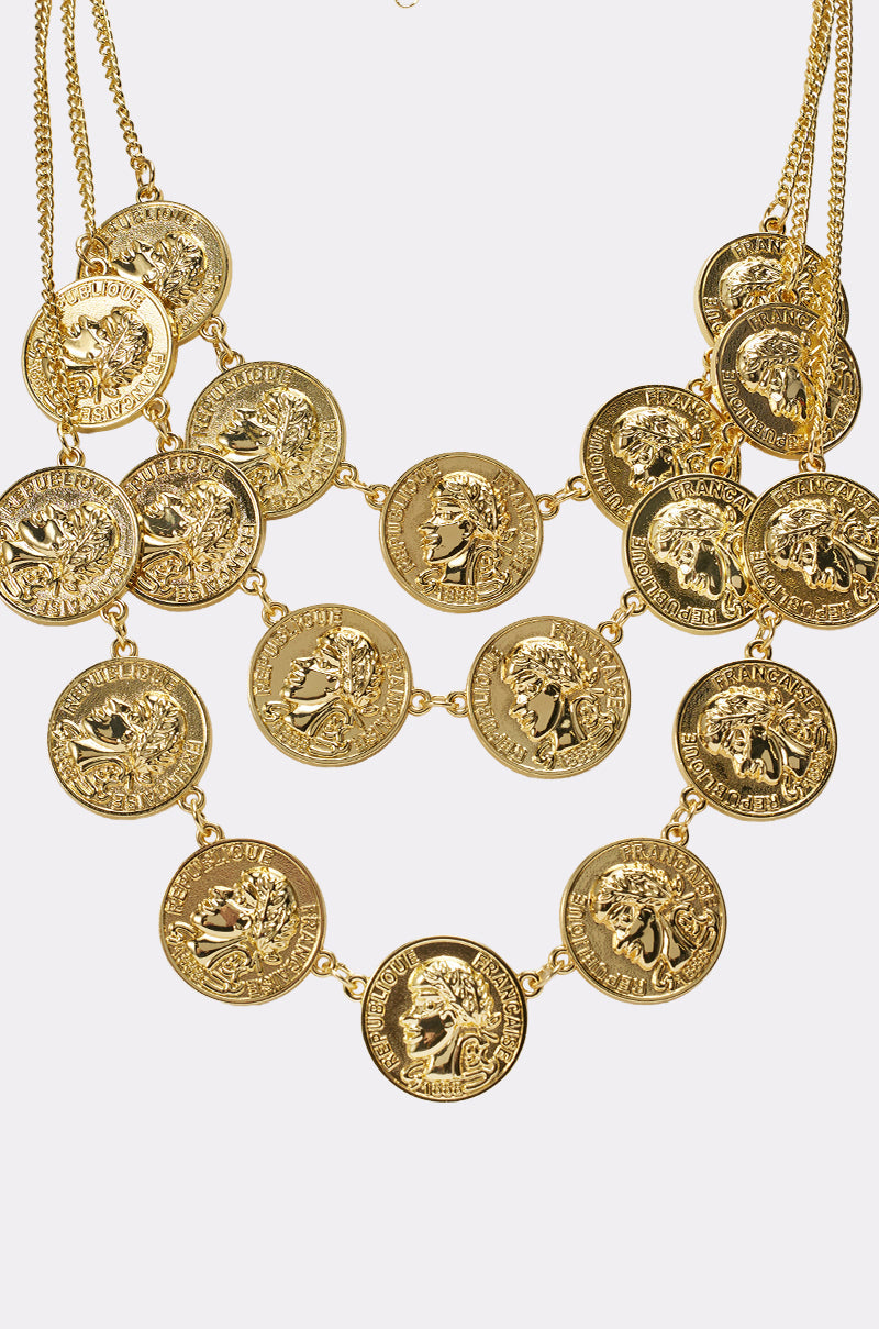 The IN MY BAG NECKLACE is a vintage-inspired layered coin necklace with multiple large, classical-style medallions on gold-tone chains, arranged in three rows with intricate detailing. 3