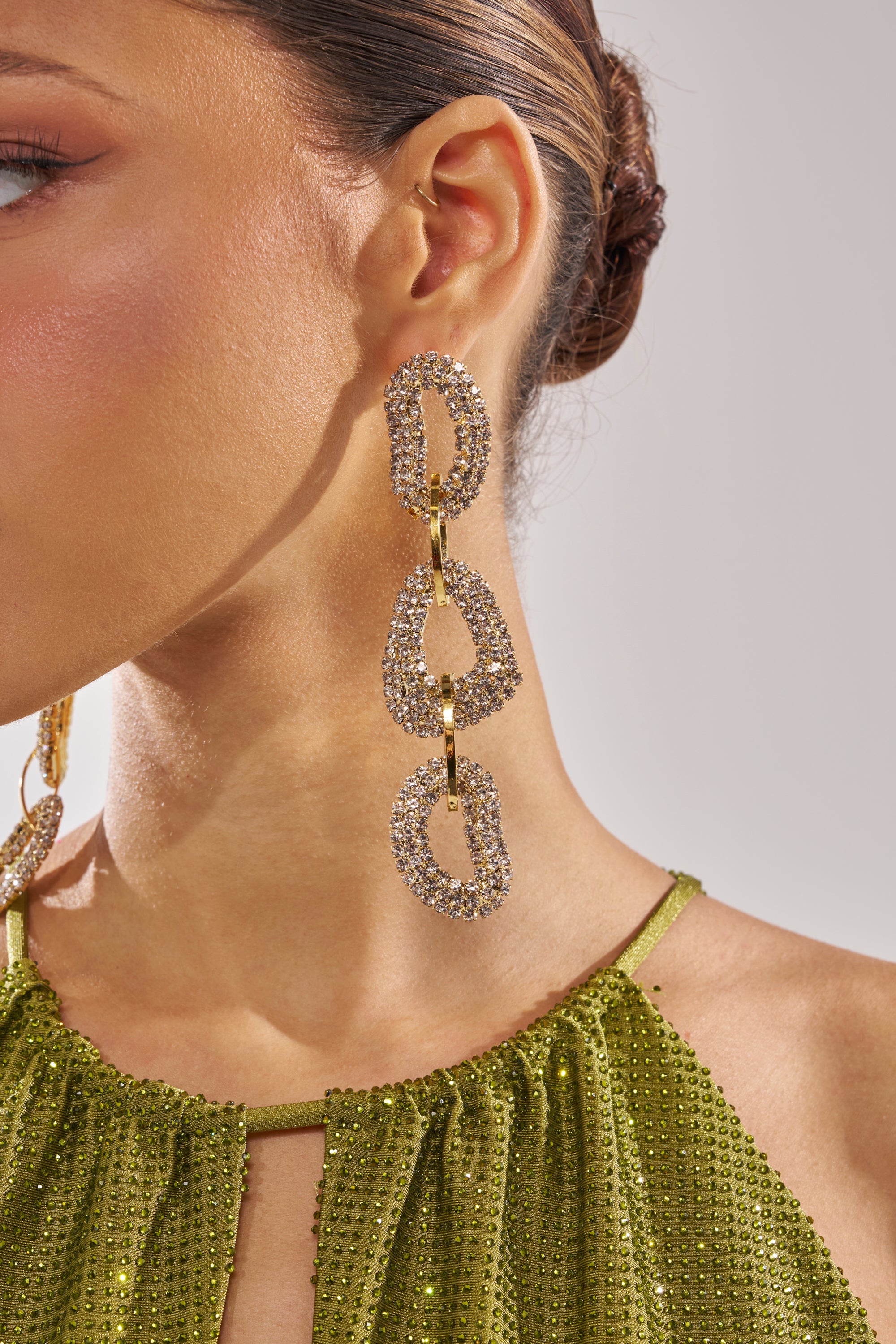 Close-up of a woman's face and shoulder, highlighting the WILD ONE EARRING—sparkling rhinestone drops—and a green beaded halter top. Her hair is in a neat updo. 2