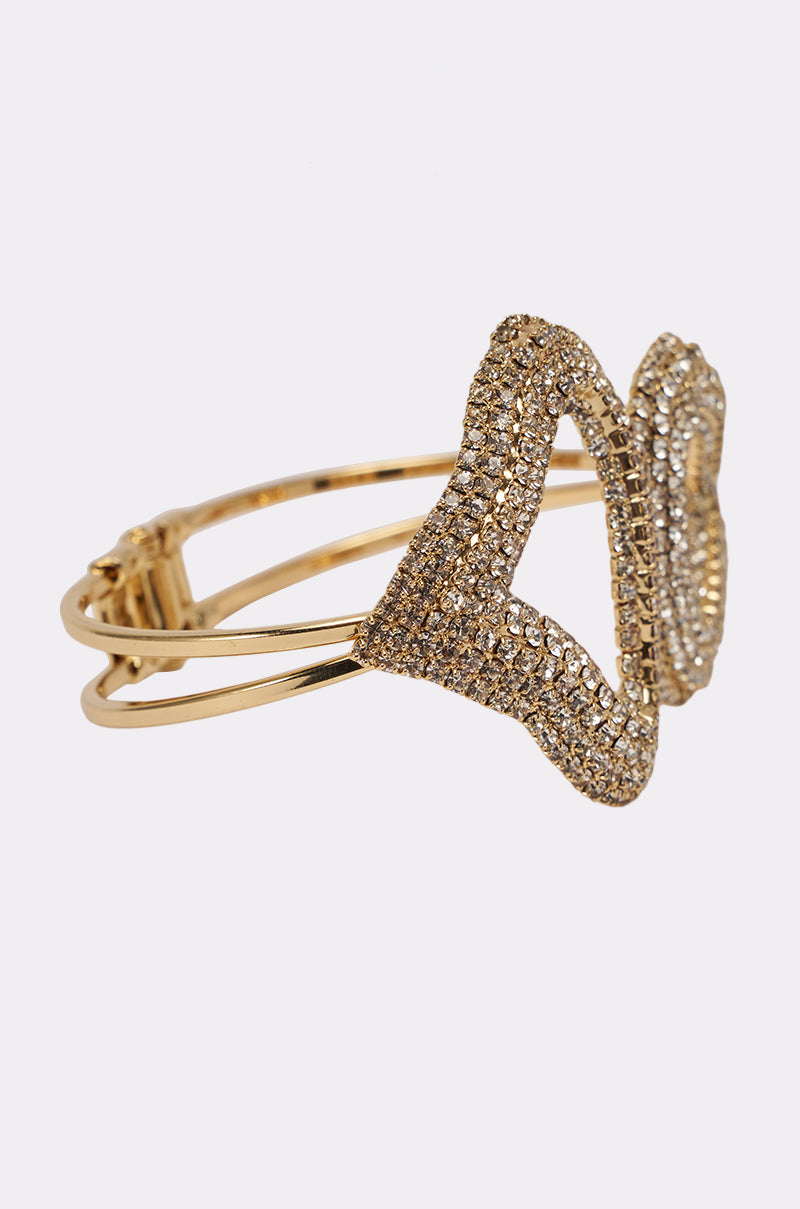 The ISNT THAT SWEET BRACELET is a gold cuff adorned with two overlapping butterfly shapes encrusted in sparkling rhinestones, displayed on a plain white background. 3